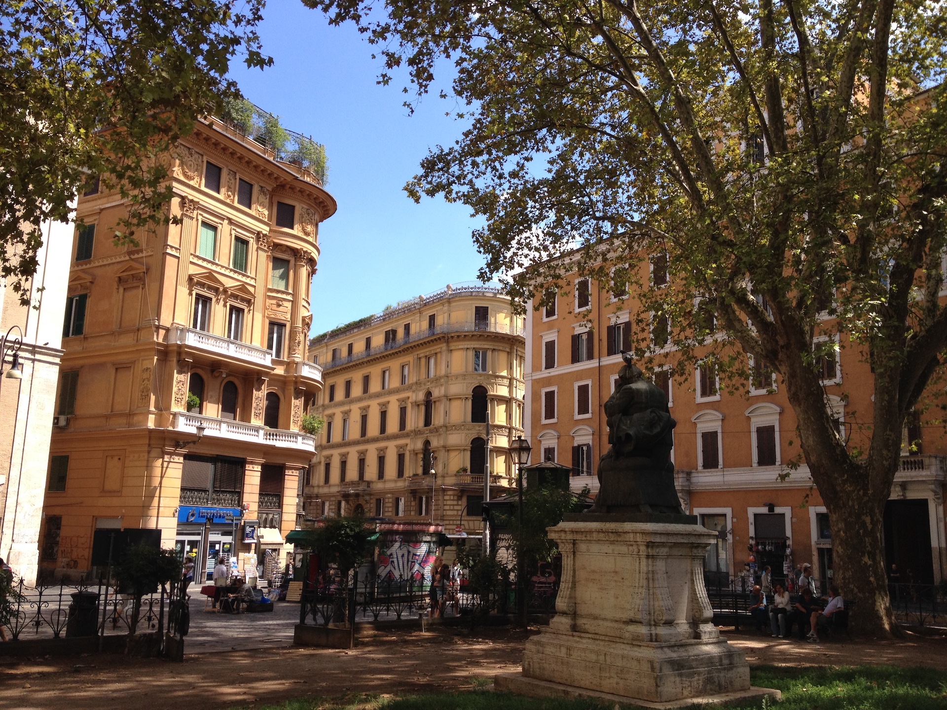 Une place ombragée de Rome entourée d'immeubles aux façades colorées de couleurs ocres