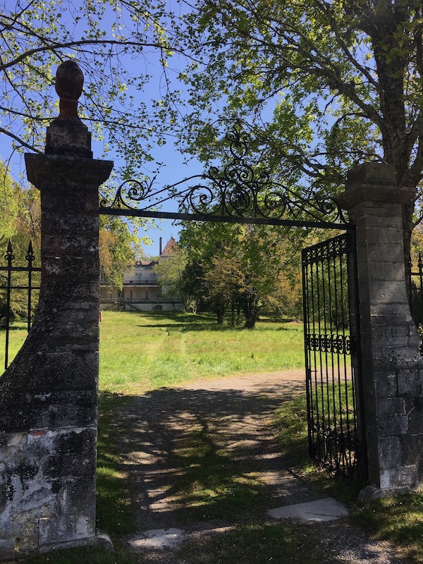 Vue sur la grille du château de Lévignacq. Elle ouvre sur un grand parc avec la bâtisse en arrière-plan